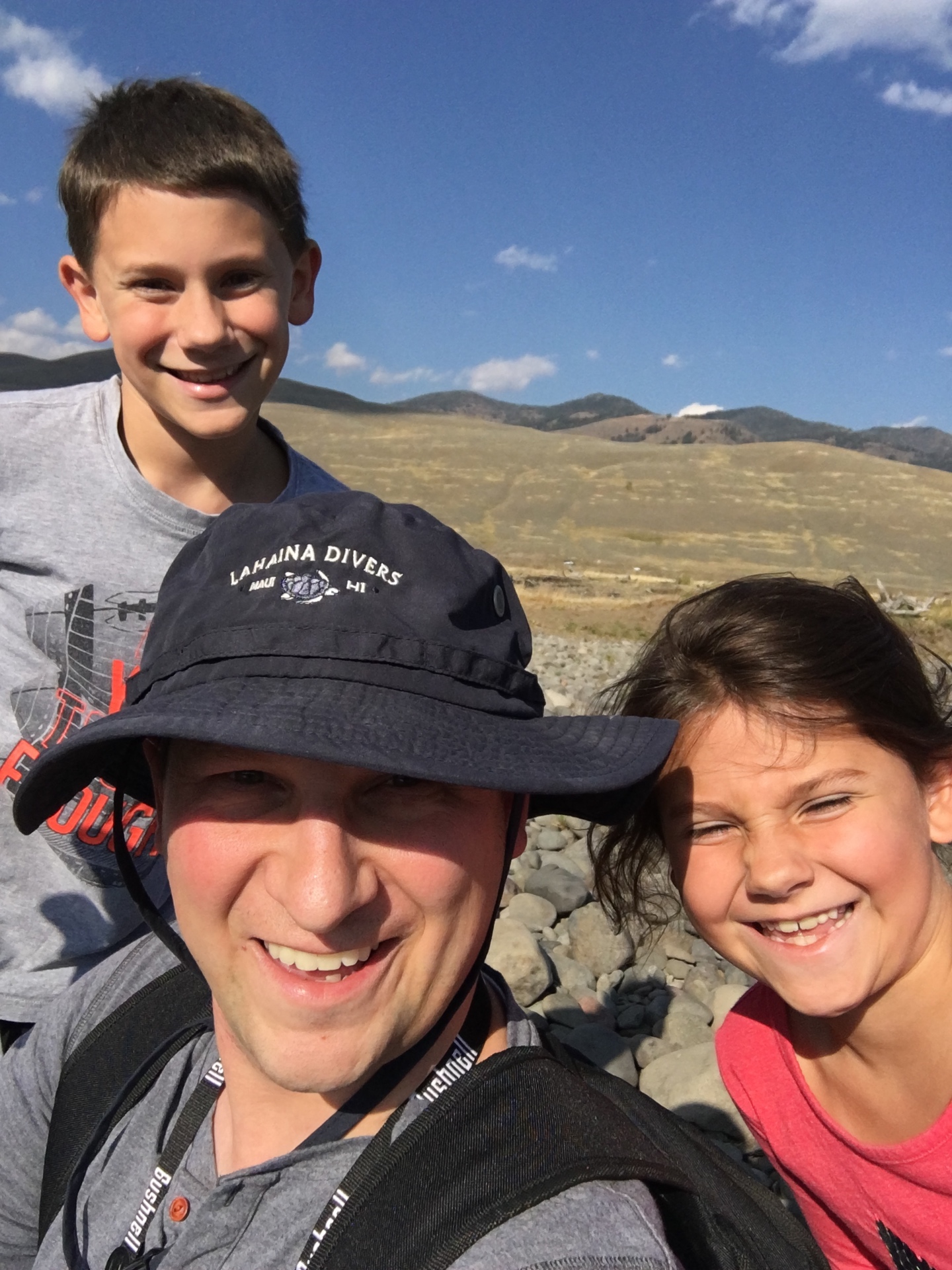 A father and two kids smiling on a hike in Yellowstone's Lamar Valley